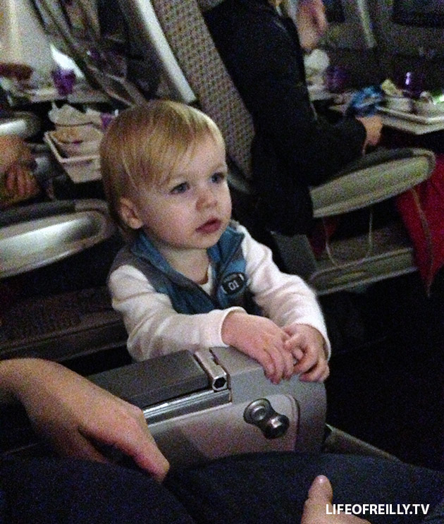 Let your little one stand in the aisle next to you. It's a long-haul flight, no-one will mind as long as they're not annoying them.